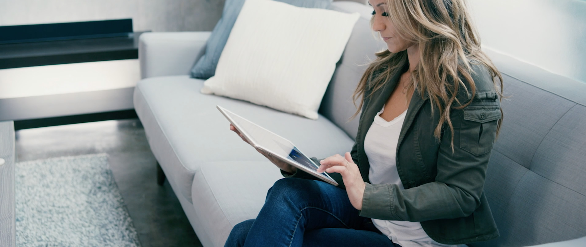 Person sitting on a light gray sofa using a tablet in a modern living room.