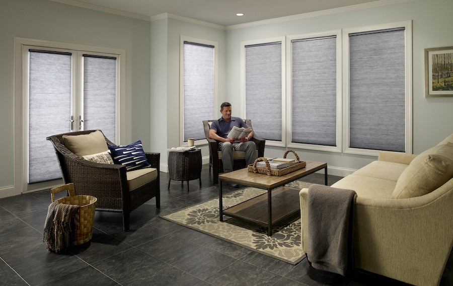 Man enjoys reading in a sunroom with motorized shades covering windows.