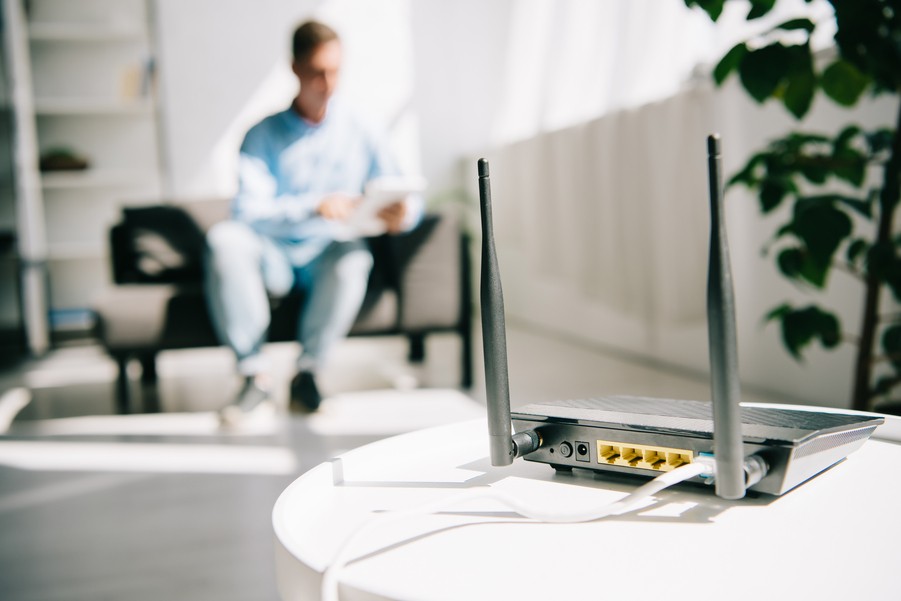 A router in the foreground, and a man using a tablet in the background.