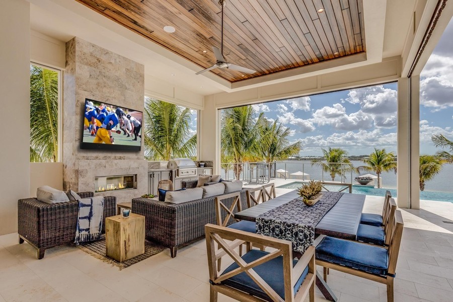 A stylish patio with a TV and fireplace beside a beach. There is an outdoor kitchen and seating area.