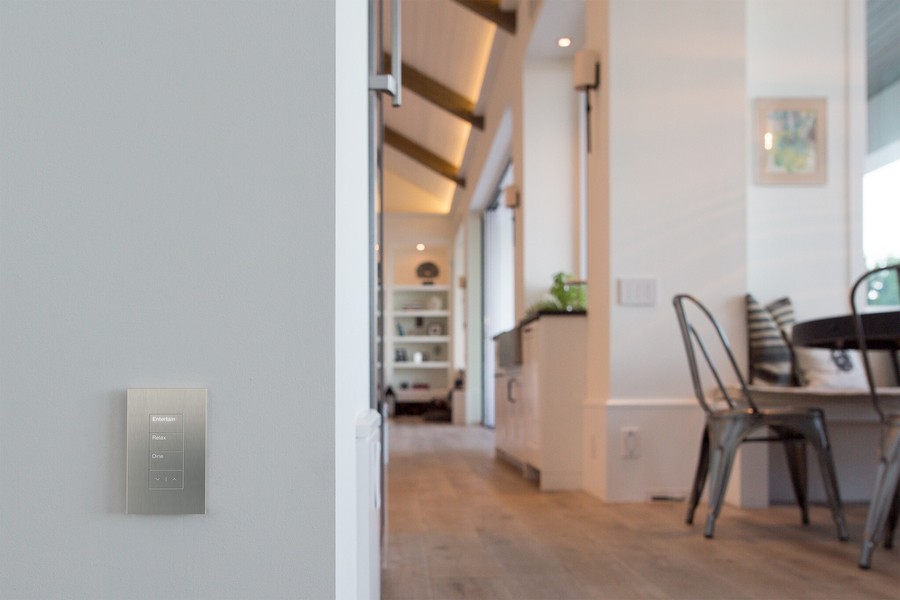 Smart lighting control panel mounted on a wall in a modern San Juan Capistrano home with a stylish dining area in the background.