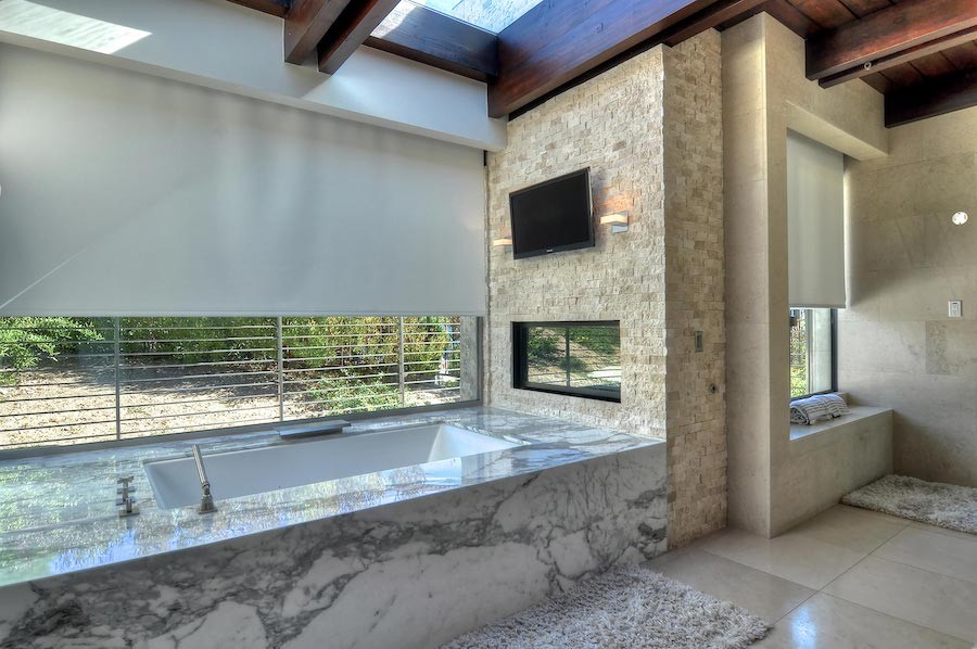 high-end bathroom with motorized shades partially lowered above a large soaking tub