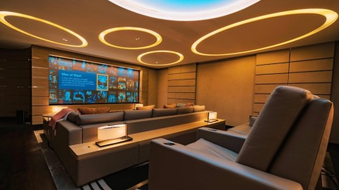 Custom home theater room with circular ceiling lights shining on tiered seating and a large display screen.