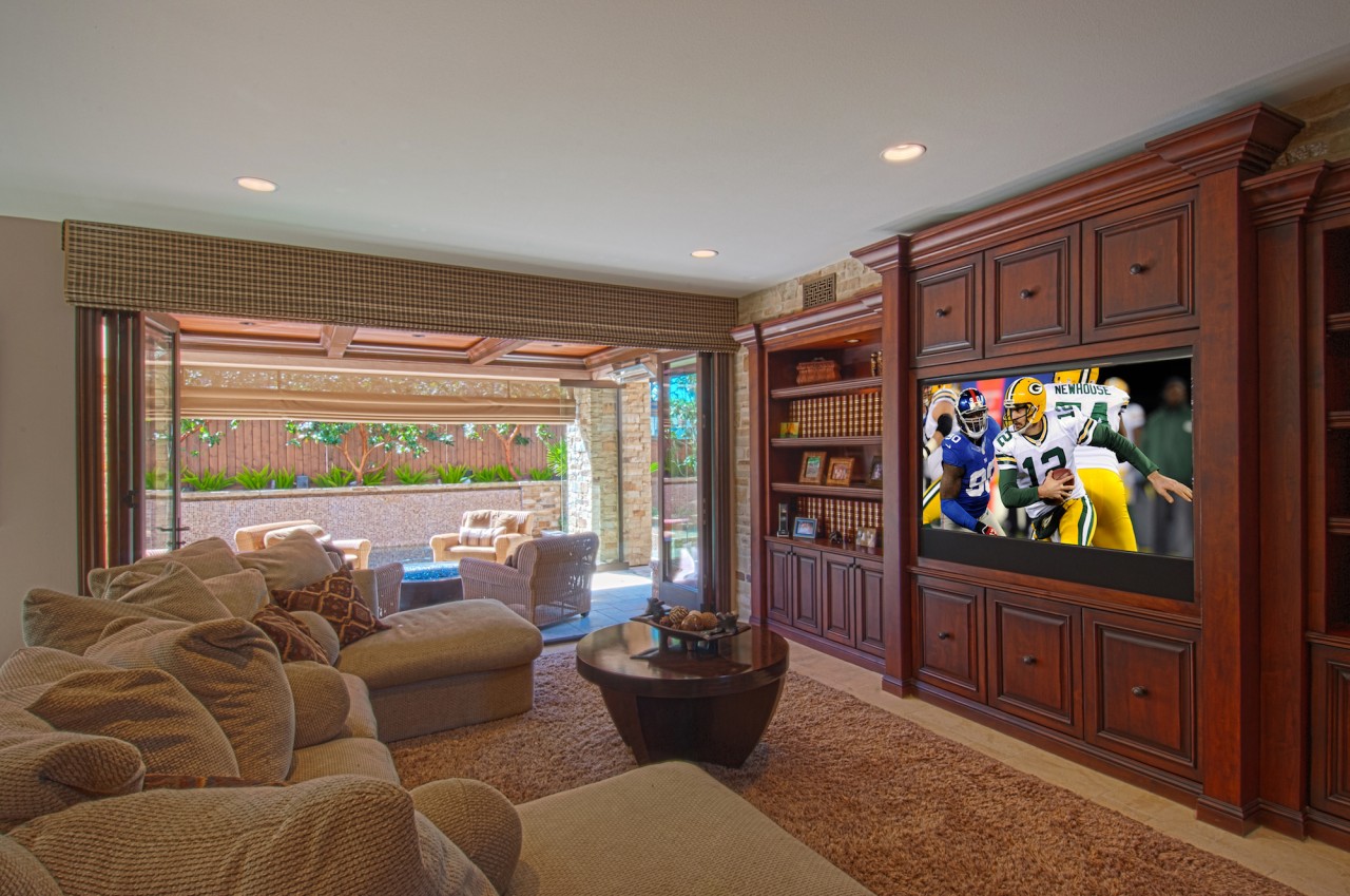 Neutral-colored living room, a football game is on the television, glass patio doors are open and it is sunny outside