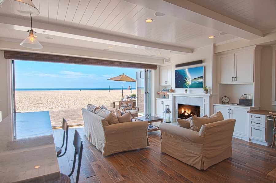 Living room with couches, a TV, and open motorized shades and a beautiful view of the beach and ocean.