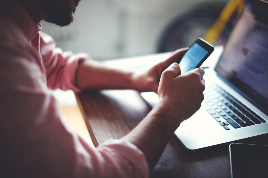 Man working with his smartphone and Wi-Fi laptop on a wooden table