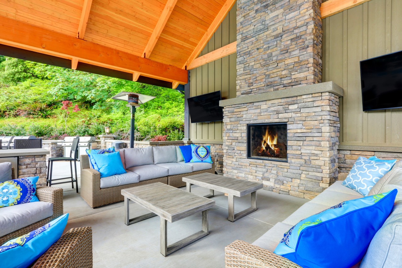 An outdoor entertainment space with TVs , lunges, a grill, and a fireplace