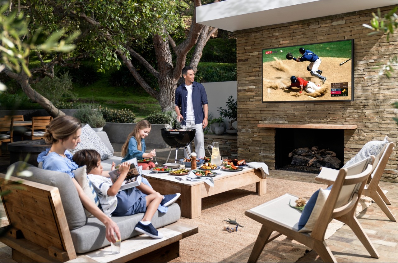 A family watching sports on an Outdoor TV installed in an open space on top of a fireplace