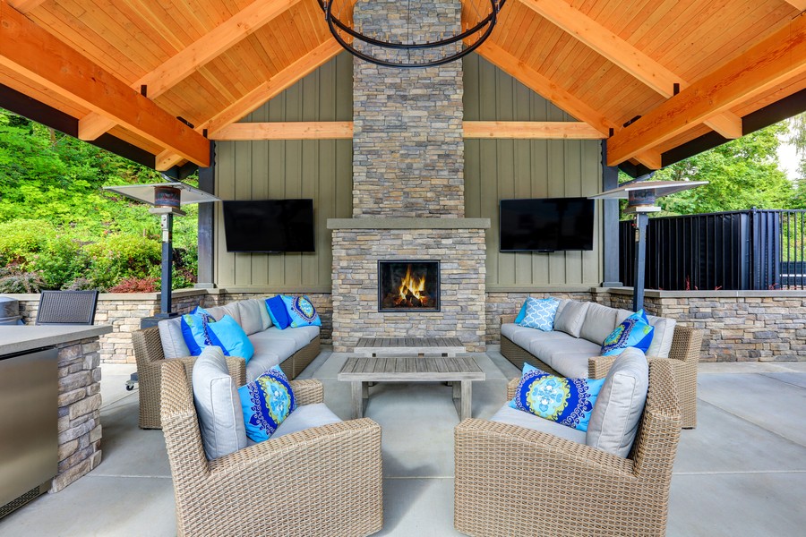 Inviting interior of covered patio area  in Tacoma Lawn Tennis Club. Stone fireplace, wicker furniture with beige cushions and bright blue pillows. Northwest, USA