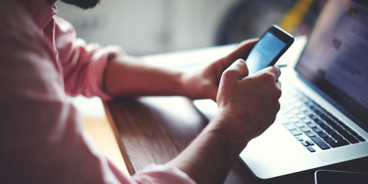 Side view shot of a man's hands using smart phone in interior, rear view of business man hands busy using cell phone at office desk, young male student texting on phone sitting at wooden table