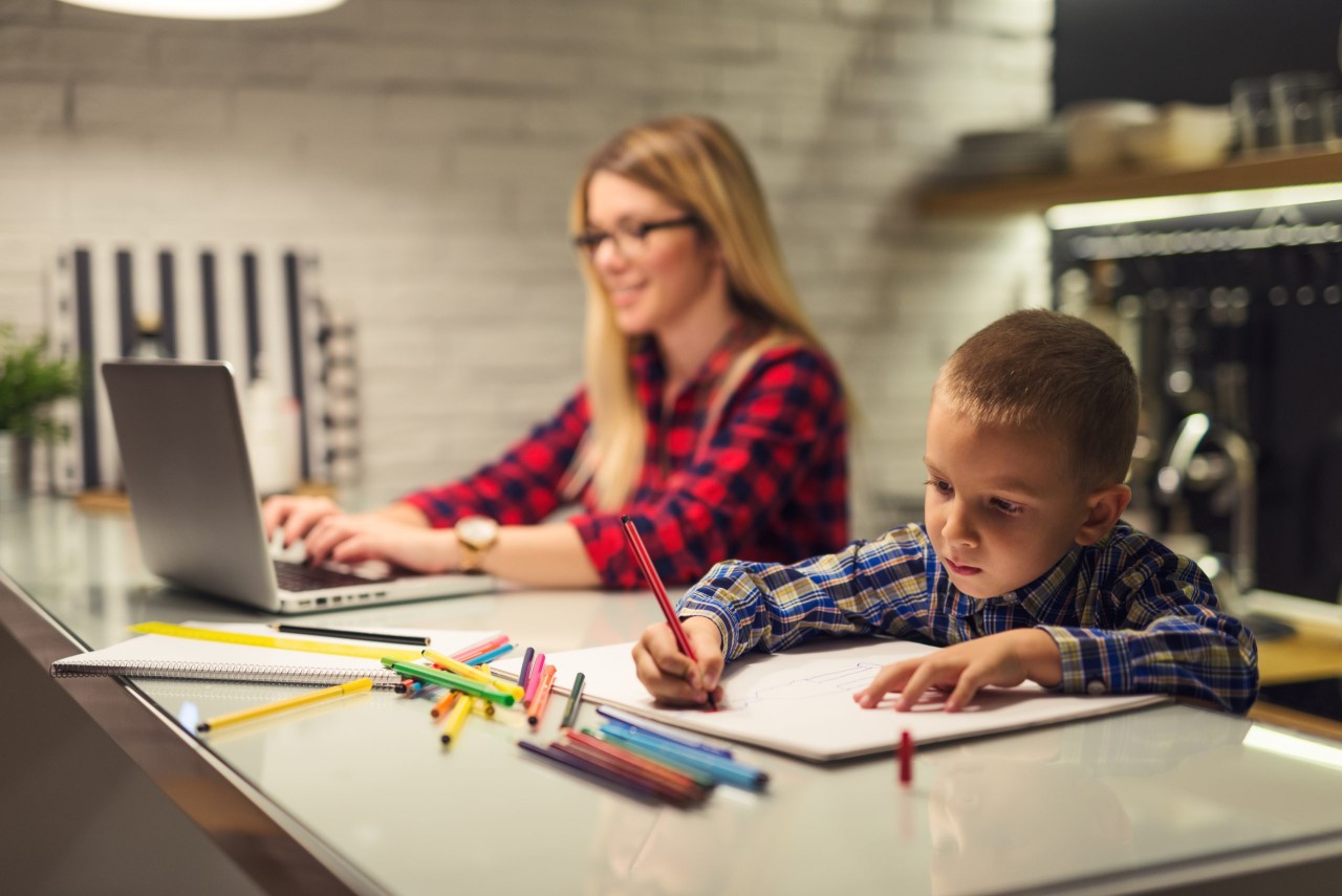 Shot of a boy drawing while his mother is working on a computer.